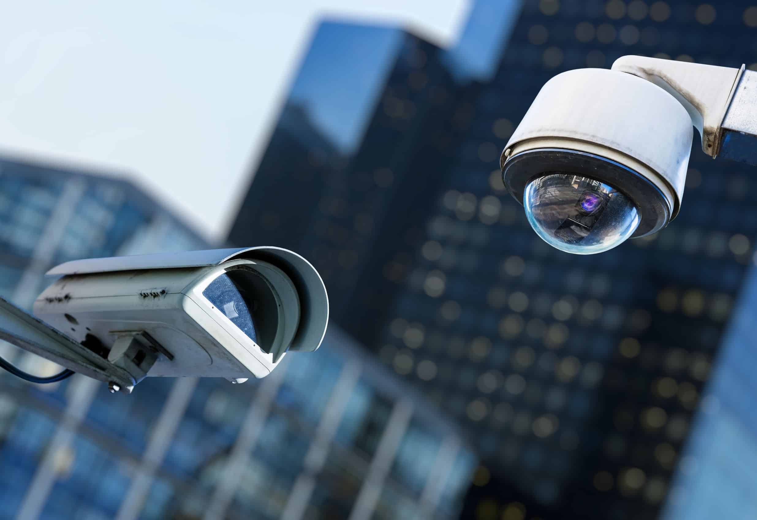 two cctv security camera in a city with blury business building on background