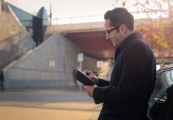 Image of a man taking notes beside a bridge.